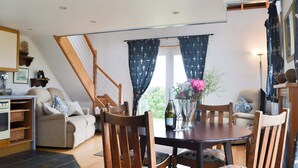 Un salon chaleureux avec une table à manger en bois, des chaises et un canapé. Un escalier mène à l’étage supérieur.