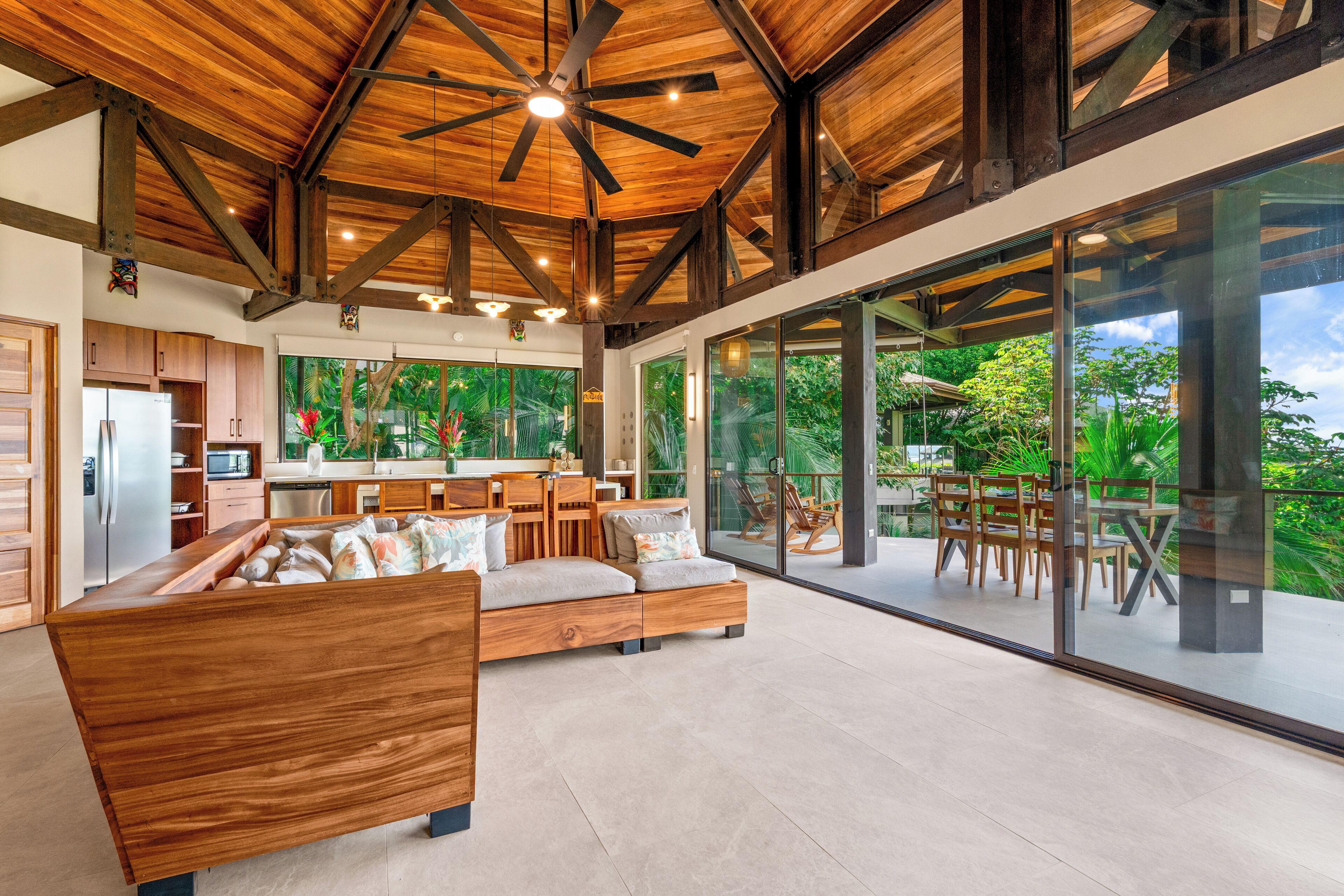 Ein geräumiger Wohnbereich mit einer Holzsofa, eine Küche mit modernen Geräten und große Glasfenstertüren, die auf einen Balkon mit Gartenmöbeln führen.