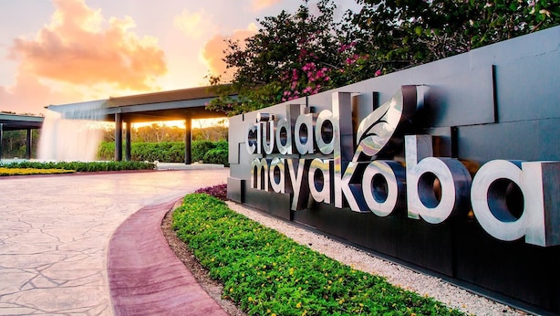 A modern building entrance with a large sign, a water feature, and landscaped areas. - CONTOY (Playa del Carmen)