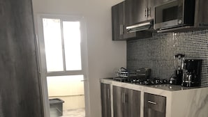 A modern kitchen with dark cabinetry, a microwave, and a coffee maker. There is a window with a view of the outside. - CONTOY (Playa del Carmen)