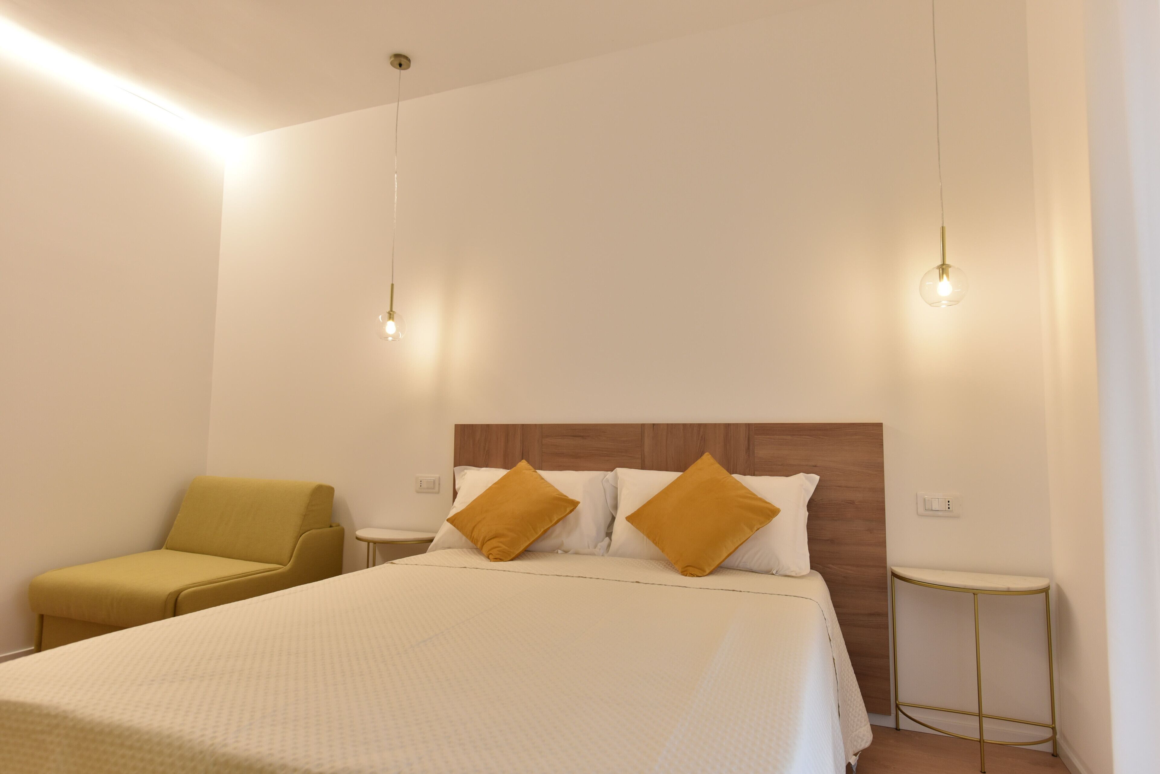 Una camera d'albergo con un letto, un comodino, una sedia e luci a sospensione.