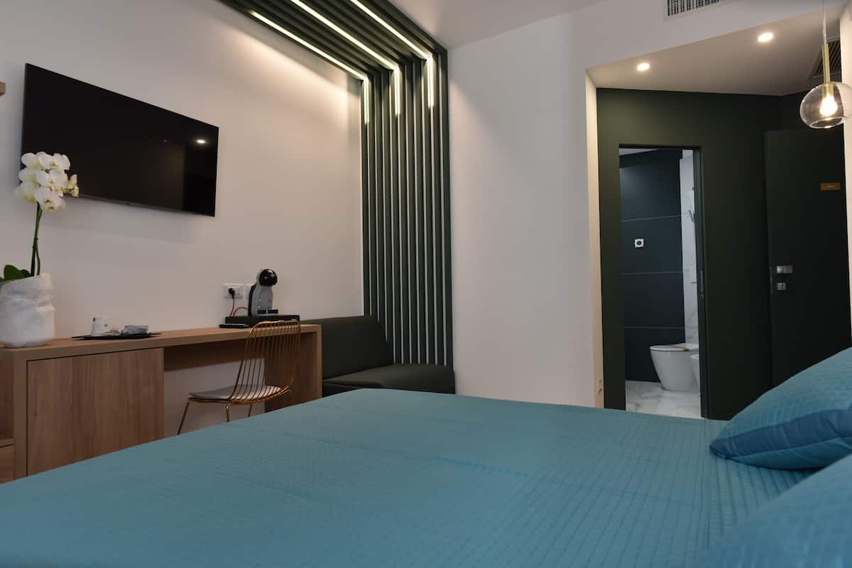 A modern bedroom with a bed, a desk, a chair, a TV, and a bathroom visible through an open door.