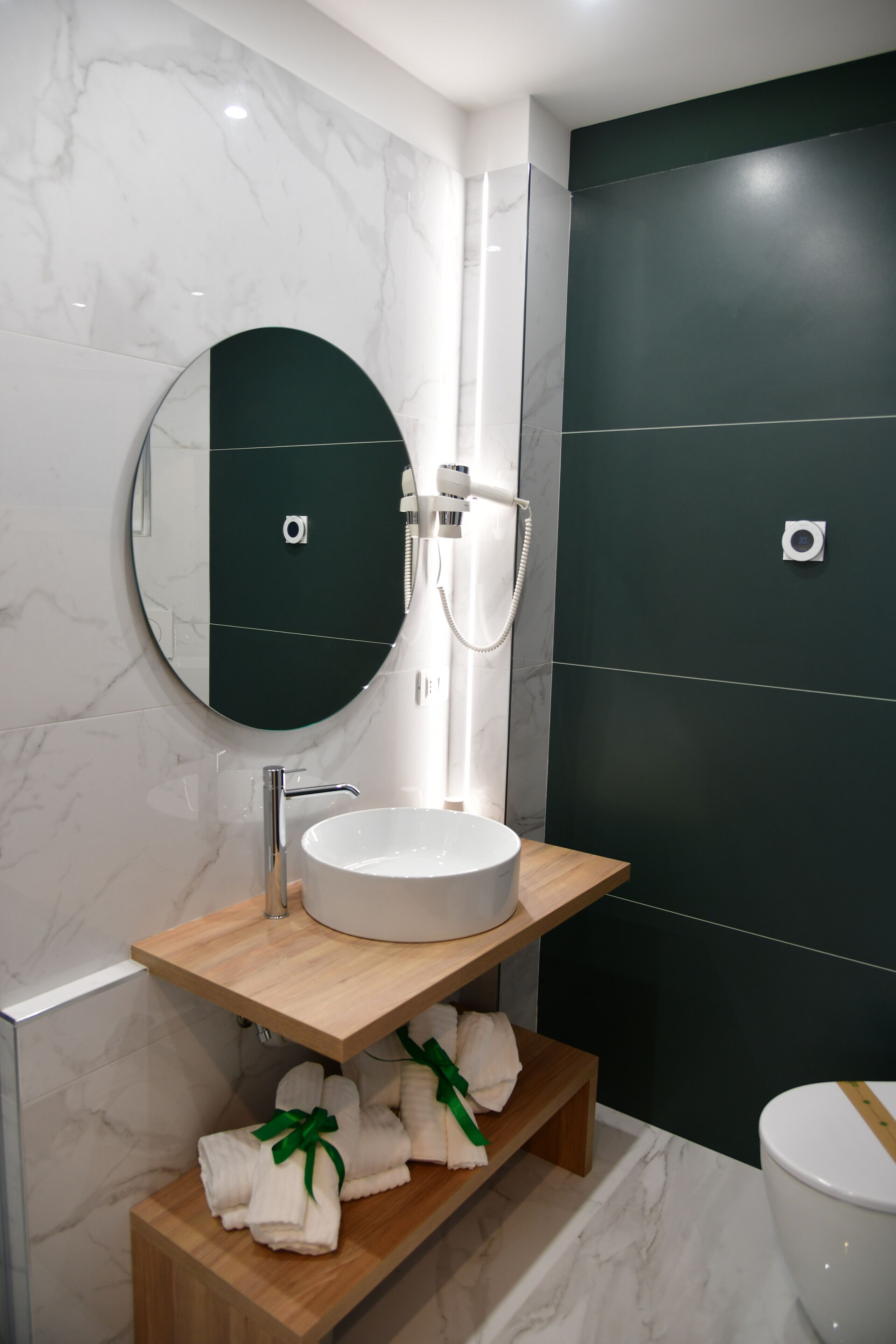 A modern bathroom with a round mirror, a white sink, and a dark-colored shower enclosure.
