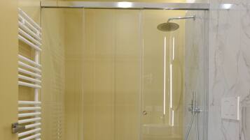 A modern bathroom with a glass-enclosed shower, a white sink, and a marble-tiled floor.
