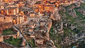 A historic town with ancient buildings perched on rocky cliffs, a prominent church tower, and a river flowing below. - Dimora al castello (Matera)