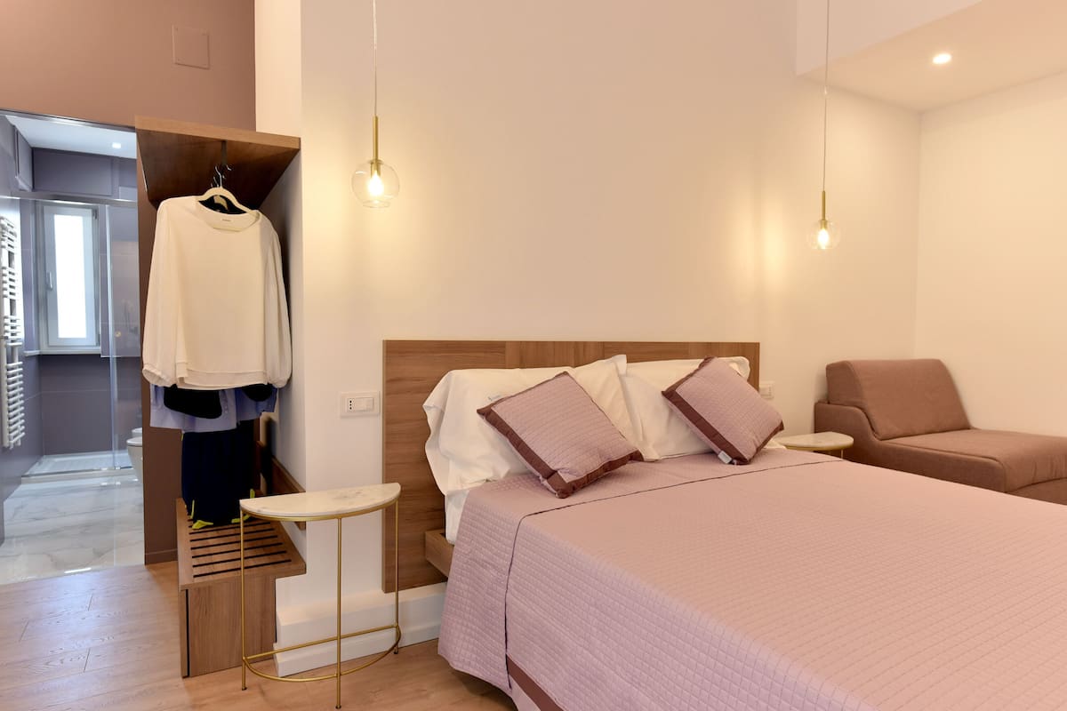 A modern hotel room with a bed, a seating area, and a clothing rack.