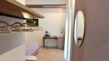 Une chambre à coucher comprenant un lit, un bureau avec une chaise, un miroir et une armoire avec des cintres.