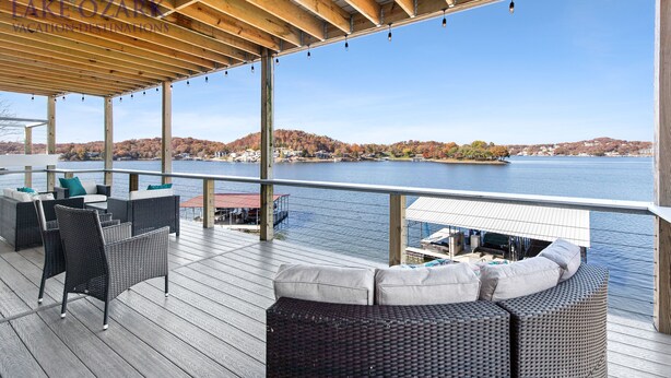 A covered deck with wicker furniture and a view of a lake and hills. - BARE FEET RETREAT! Swim Dock, 5 Decks, Elevator, Gaming Room, Bagnell Dam Strip! (Lake Ozark)