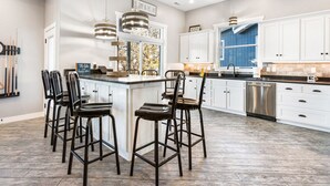 A kitchen with a central island, bar stools, white cabinets, and a stainless steel dishwasher. - BARE FEET RETREAT! Swim Dock, 5 Decks, Elevator, Gaming Room, Bagnell Dam Strip! (Lake Ozark)