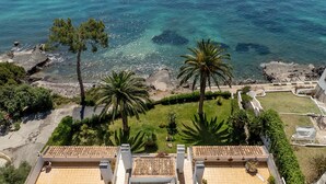 A rooftop terrace with a view of the sea, palm trees, and a tiled roof.