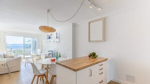 A modern kitchen with a wooden countertop, white cabinetry, and a dining area with a white table and chairs.