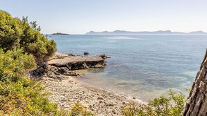 A coastal landscape with rocky terrain, clear water, and distant mountains.