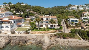 A coastal residential area with houses, a clear view of the sea, and a rocky shoreline.