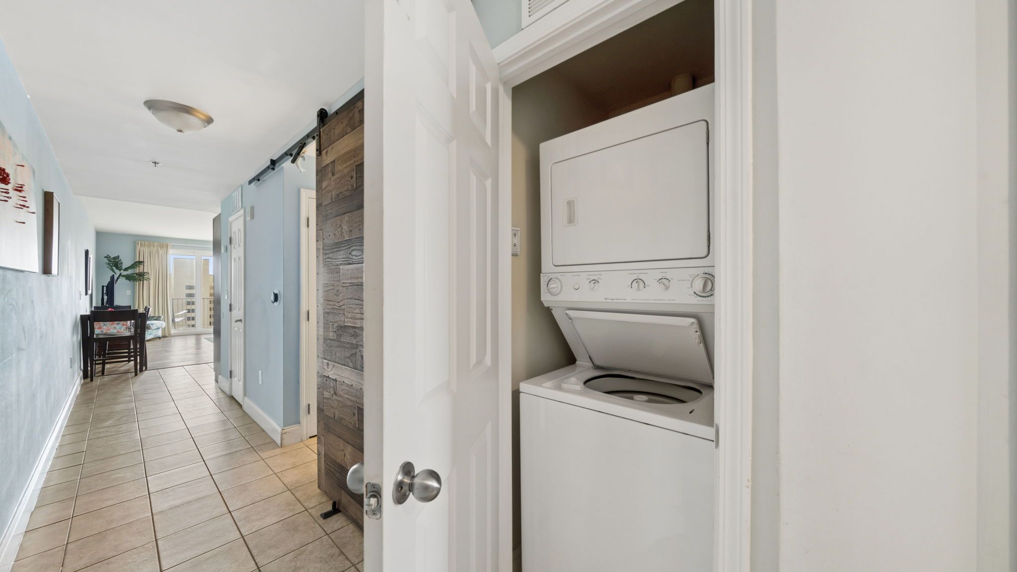 A laundry room with a front-loading washer and dryer, a wooden door, and a tiled floor.