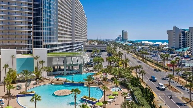 A hotel with a large pool, palm trees, and a view of the beach. - Sand n Stars (Panama City Beach)