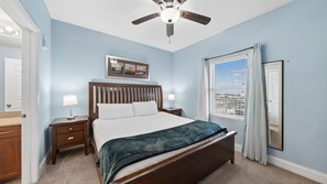 A bedroom with a bed, nightstands, a ceiling fan, a window with curtains, and a door.