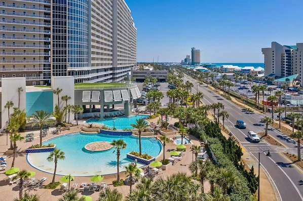 A resort with a large central pool, multiple buildings, and a road with vehicles.