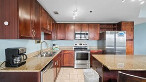 Una cocina con armarios de madera, electrodomésticos de acero inoxidable, una cafetera y un cubo de basura.