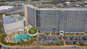 A large hotel with a modern glass facade, a swimming pool complex, and a parking area. - Sand n Stars (Panama City Beach)