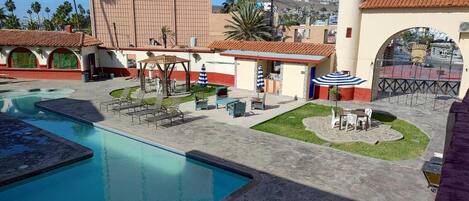 A pool area with lounge chairs and umbrellas, a building with a tiled roof, and a gate with a decorative arch.