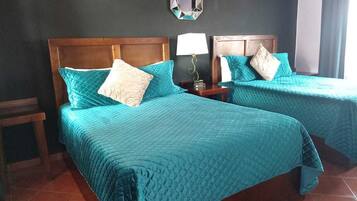 A hotel room with two beds, each with a wooden headboard, a nightstand with a lamp, and a wall-mounted air conditioner.