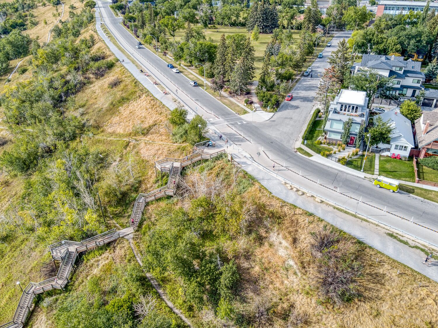 Vue aérienne d’une zone résidentielle en périphérie, avec une route, un pont piétonnier et des maisons.