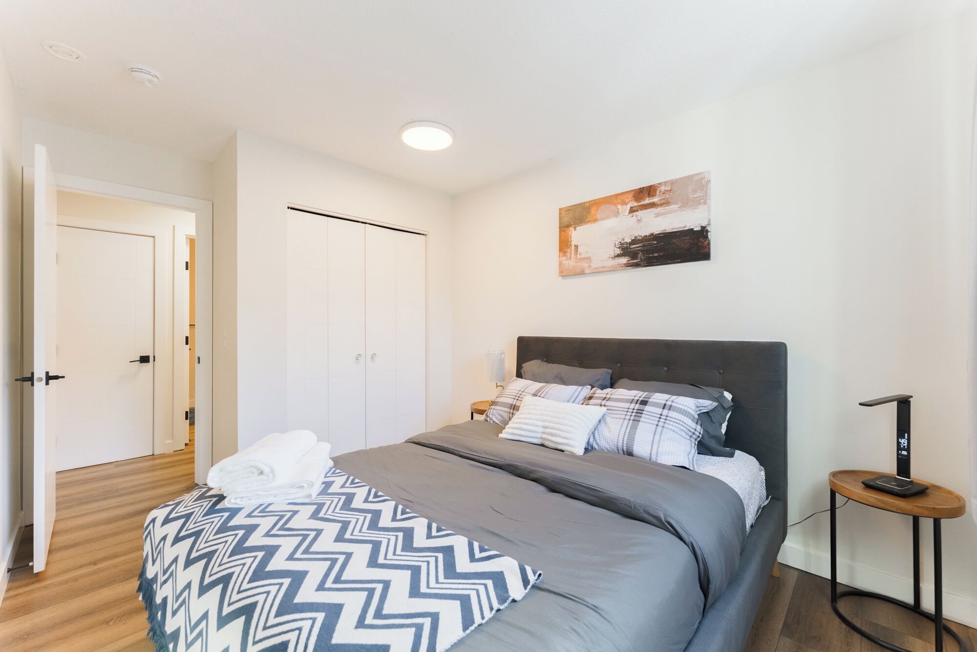 Ein Schlafzimmer mit einem Bett, Kissen, einem Nachttisch, einer Wanduhr und einer Tür.