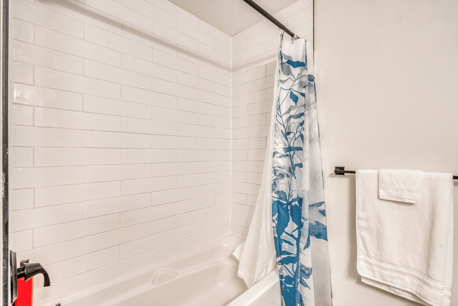 Um banheiro com paredes revestidas de azulejos brancos, chuveiro com cortina azul e branca, e uma toalha branca pendurada em um suporte.