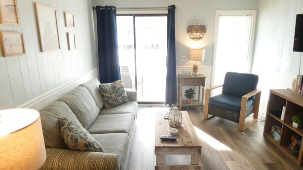 Una sala de estar con un sofá, una mesa de centro, una silla, una lámpara y un televisor.