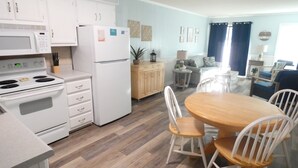 Una cocina moderna con electrodomésticos blancos, un comedor con mesa de madera y sillas blancas, y una sala de estar con sofá y mesa de centro.