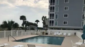 Una piscina con tumbonas y un edificio al fondo.