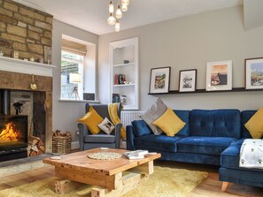 A living room with a fireplace, a blue sofa, a wooden coffee table, and a bookshelf. - 4 bedroom accommodation in Holmfirth (Holmfirth)