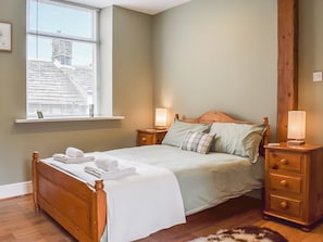 A bedroom with a wooden bed, bedside lamps, a window with blinds, and a view of buildings outside. - 4 bedroom accommodation in Holmfirth (Holmfirth)