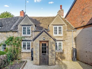 A stone building with a wooden door, two windows, and a chimney. - A charming and characterful Cotswold cottage in the heart of a quaint village. (Milton-Under-Wychwood)