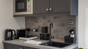 Ett modernt kök med gråa skåp, en mikrovågsugn i rostfritt stål, en kaffebryggare och en diskho.