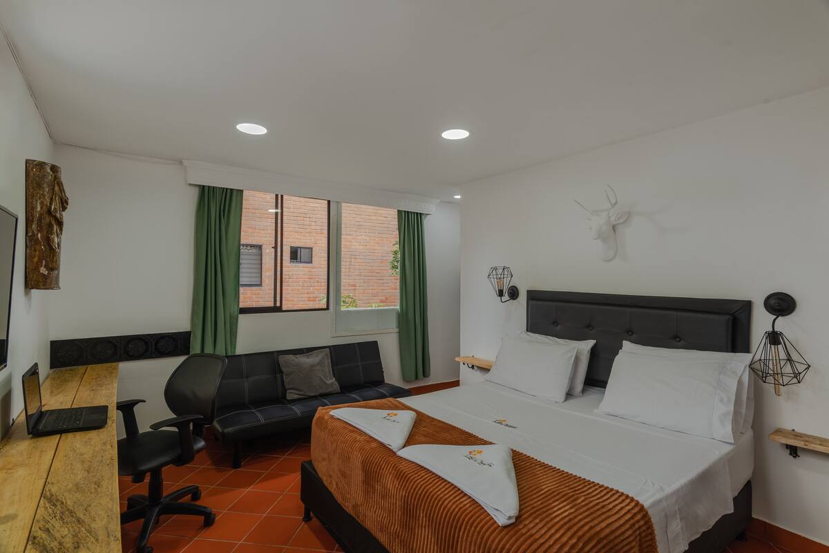 Une chambre d’hôtel avec un lit, un bureau, une chaise et une fenêtre avec des rideaux.