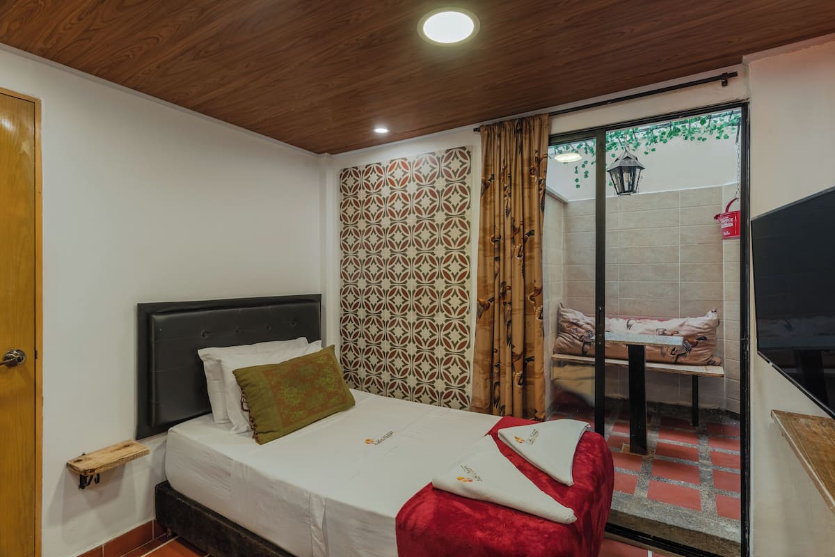 Une chambre à coucher avec un lit, une table de chevet, une fenêtre avec des rideaux et une vue sur l’extérieur.