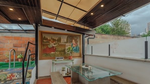 A patio area with a glass table, a bench, a mural, and a brick wall.