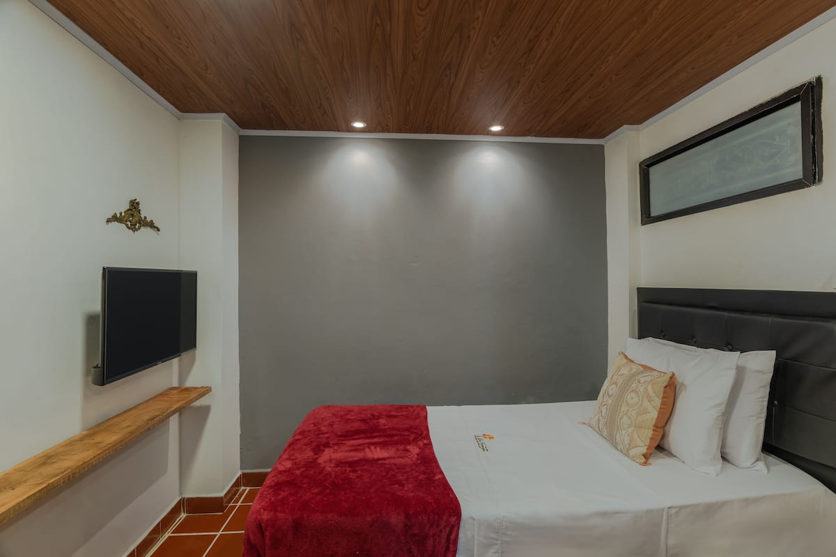 Une chambre à coucher avec un lit, un téléviseur fixé au mur, un plaid rouge et une tête de lit.