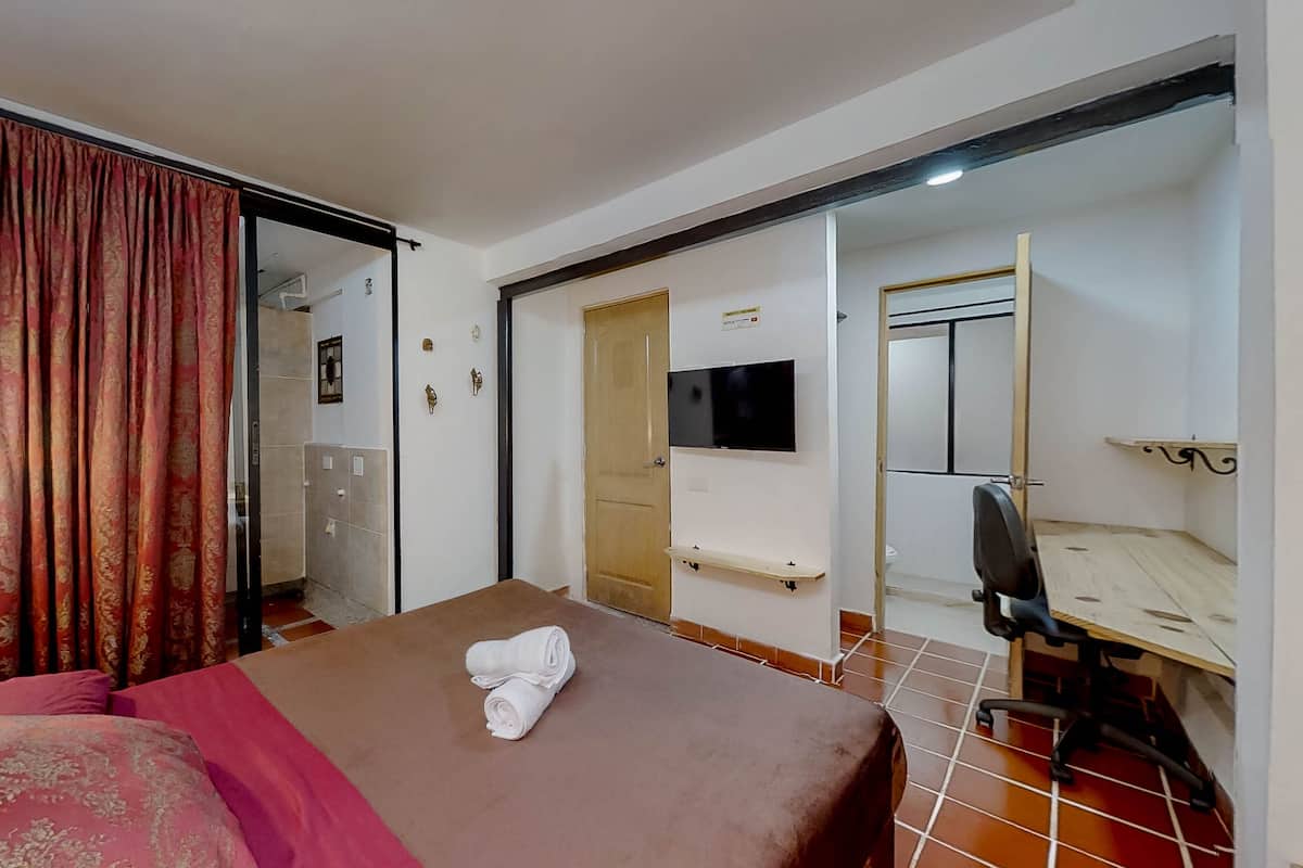 Une chambre d’hôtel avec un lit, un bureau, une chaise, une télévision et une salle de bain visible à travers une porte ouverte.