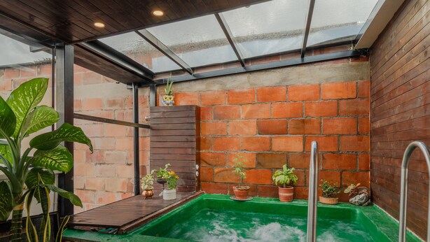 A spa area with a green hot tub, tiled walls, and potted plants.