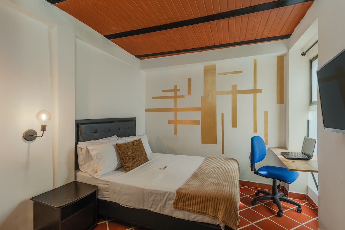 Une chambre à coucher avec un lit, un bureau avec un ordinateur portable, une chaise et un mur orné de motifs géométriques.