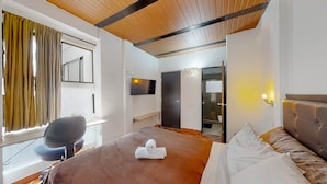 A hotel room with a large bed, a desk, a chair, a television, and a bathroom visible through an open door.