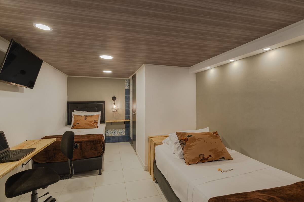 Une chambre à coucher avec un lit, un bureau avec un ordinateur portable, une chaise et un téléviseur fixé au mur.