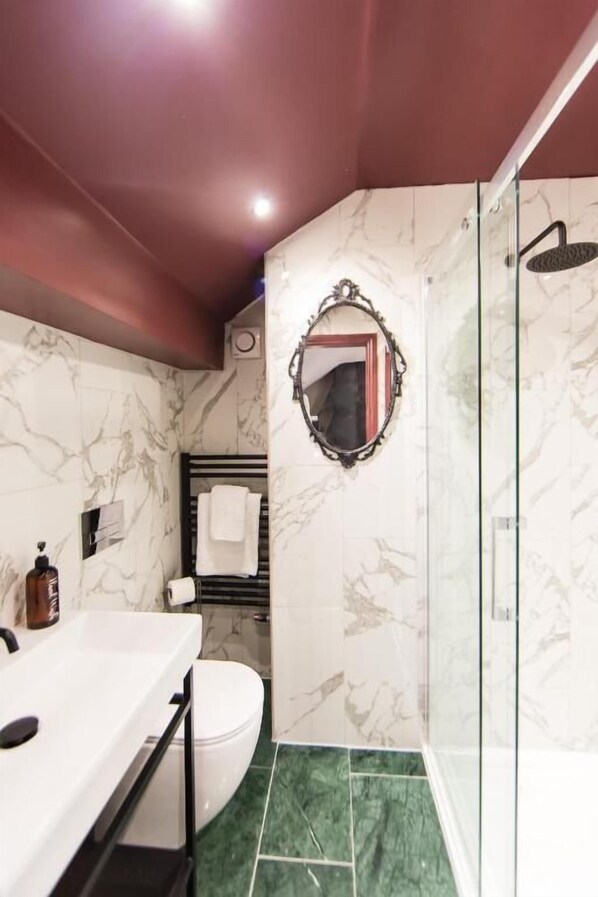 Une salle de bain moderne avec un mur en marbre, une douche en verre et un lavabo blanc.
