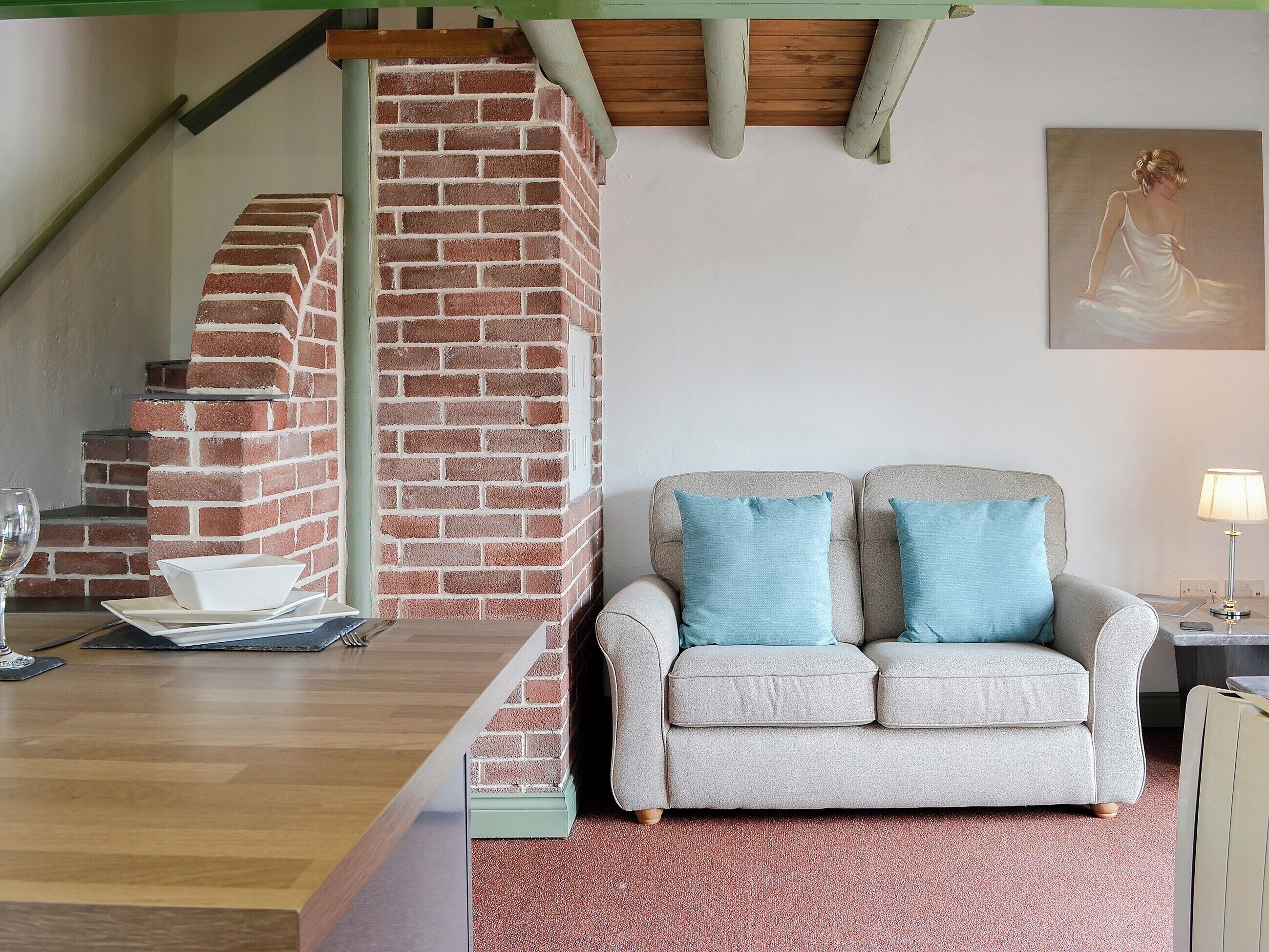 A living room with a brick fireplace, a sofa with blue cushions, and a dining area with a table and chairs.