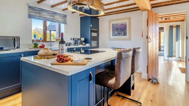A modern kitchen with a central island, blue cabinetry, and wooden beams on the ceiling.