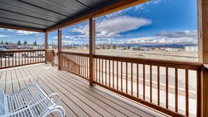 A covered outdoor area with a wooden deck, metal chairs, and a view of a snowy mountain range and buildings in the distance. - Midgarth Hus- Brand New PET FRIENDLY home minutes to Copper & Ski Cooper! (Leadville)