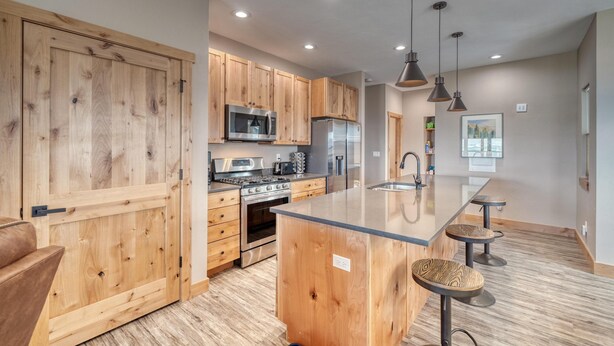 A modern kitchen with wooden cabinets, stainless steel appliances, and a central island with bar stools. - Midgarth Hus- Brand New PET FRIENDLY home minutes to Copper & Ski Cooper! (Leadville)