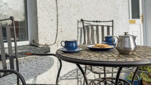 Een ronde metalen tafel met een metalen stoel, een blauwe kop, een bord met koekjes en een metalen pot.